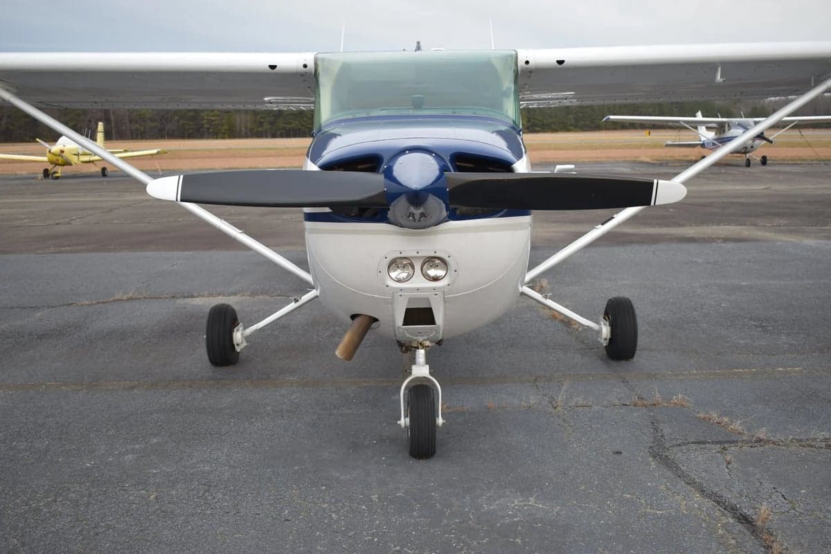 A close-up front view of the propeller, nose, and landing gear of a white and blue Cessna 172.