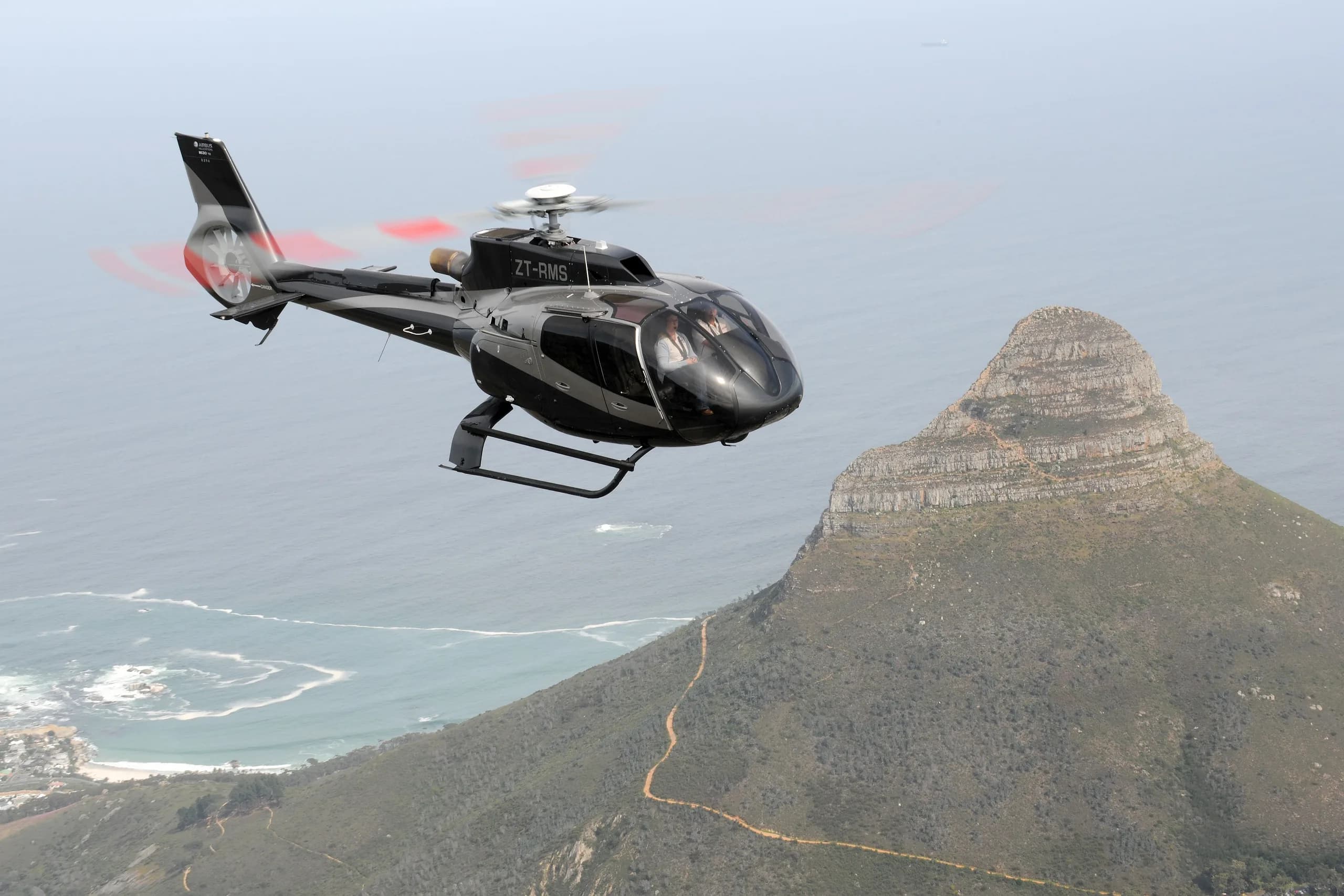 Black Eurocopter EC135 flying near a mountain.