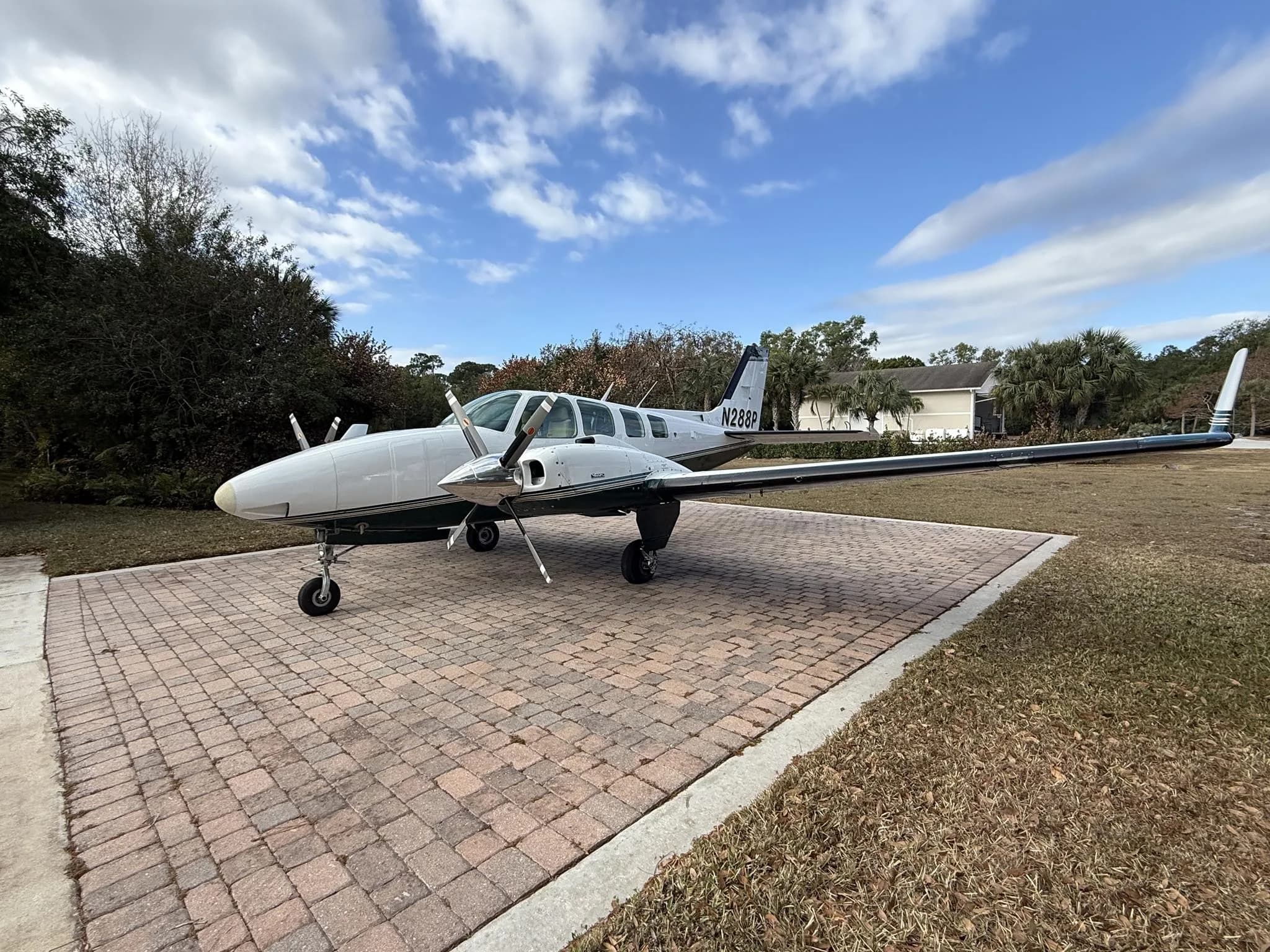 A white and green twin-engine Beechcraft Baron aircraft with tail number N288P parked on a brick driveway, viewed from the left side.