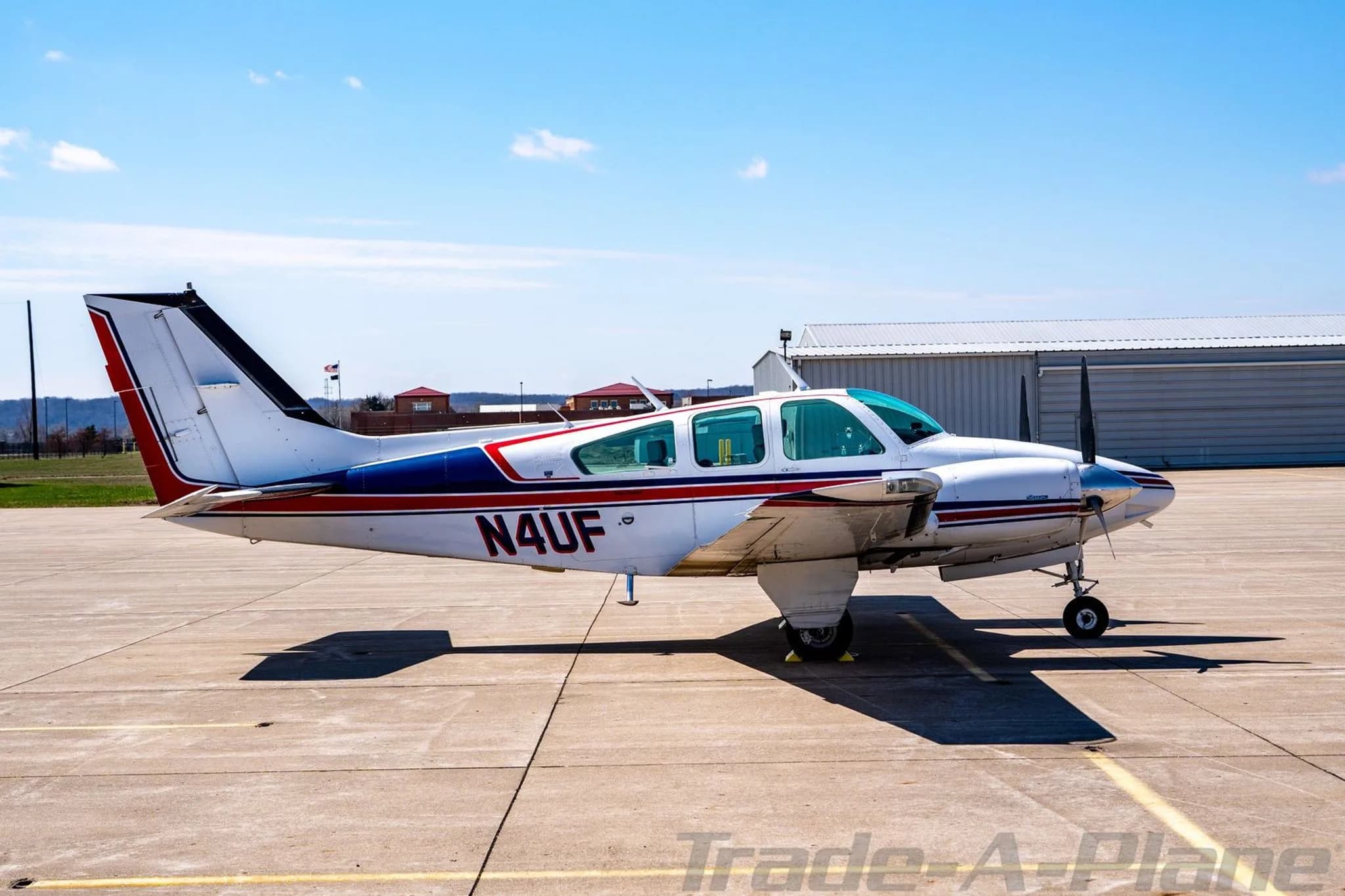 Side view of the N4UF twin-engine Beechcraft Baron with red and blue stripes on a sunny day.