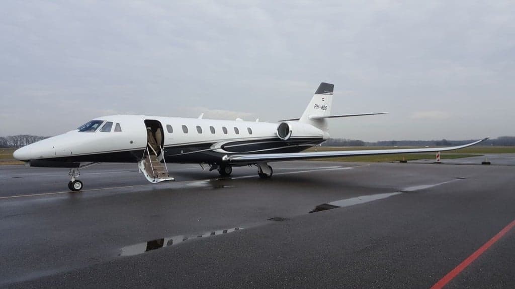 A white and black private jet parked on the tarmac with the door open and stairs extended.