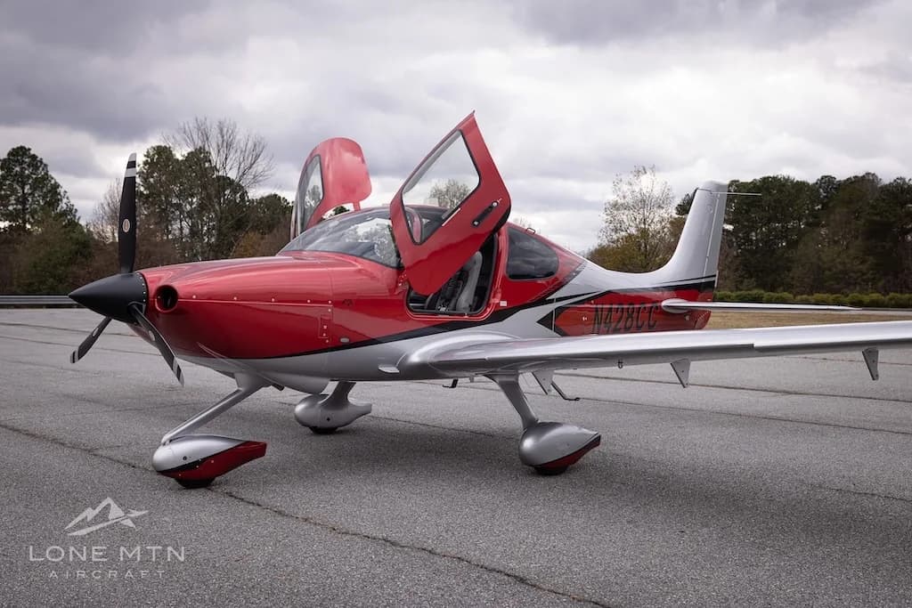 A red and silver Cirrus Vision Jet (N428CC) with its gull-wing doors open, parked on an asphalt tarmac.