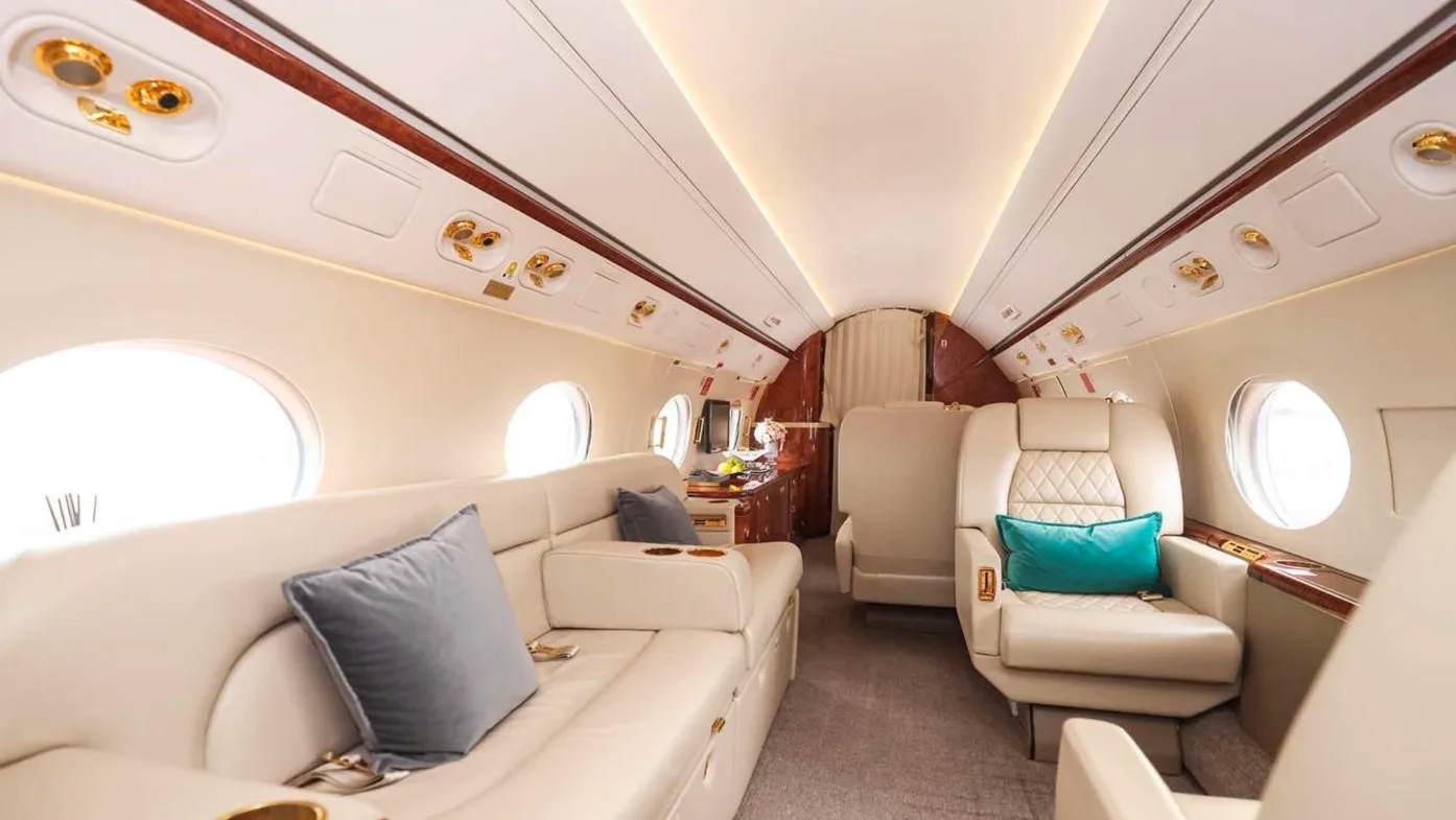 Interior of a private jet with white leather seating and wood trim.