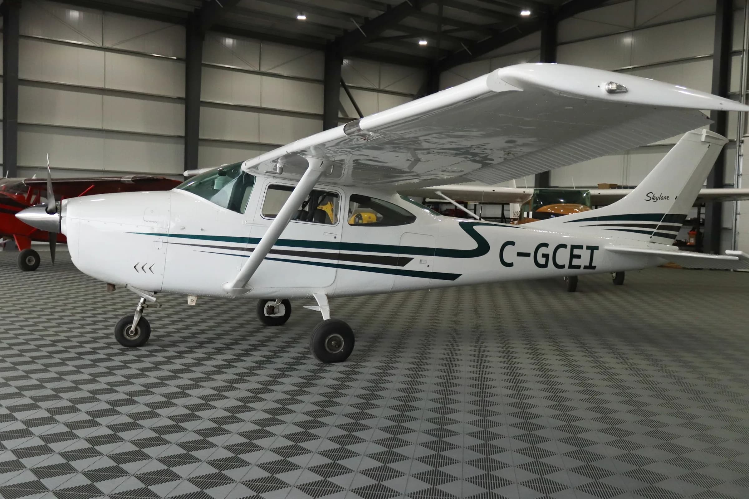 A white Cessna Skylane with dark green and black stripes is parked in a hangar, viewed from the side.