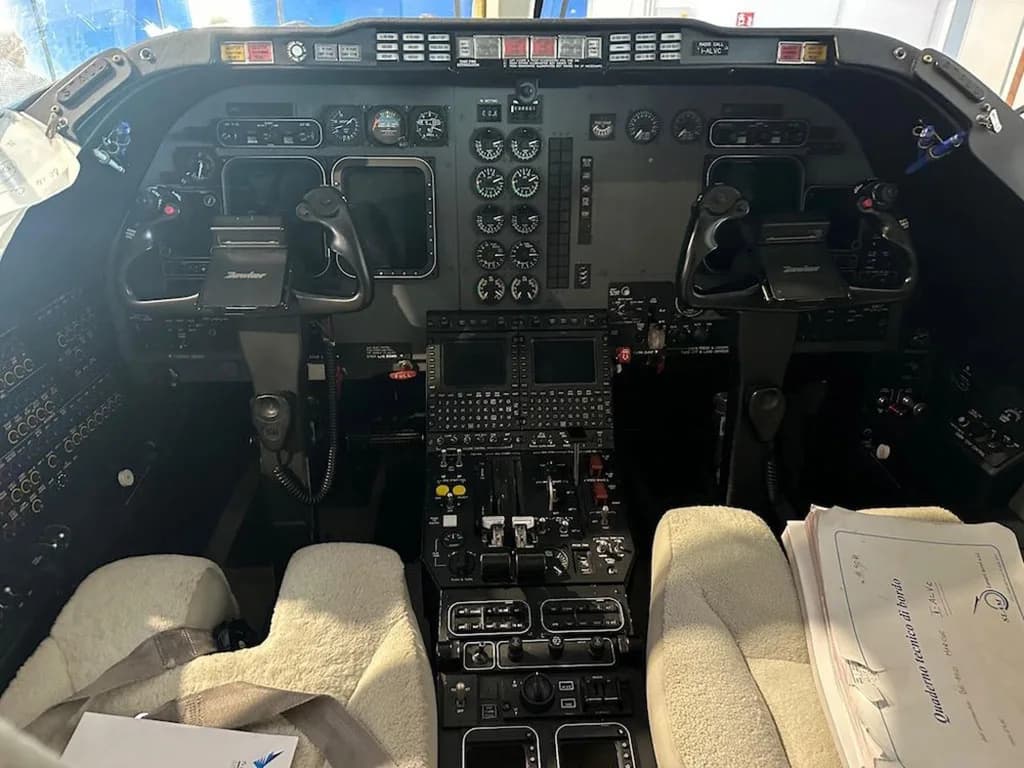 The cockpit of a private jet features a complex instrument panel with multiple gauges, screens, and two control yokes.