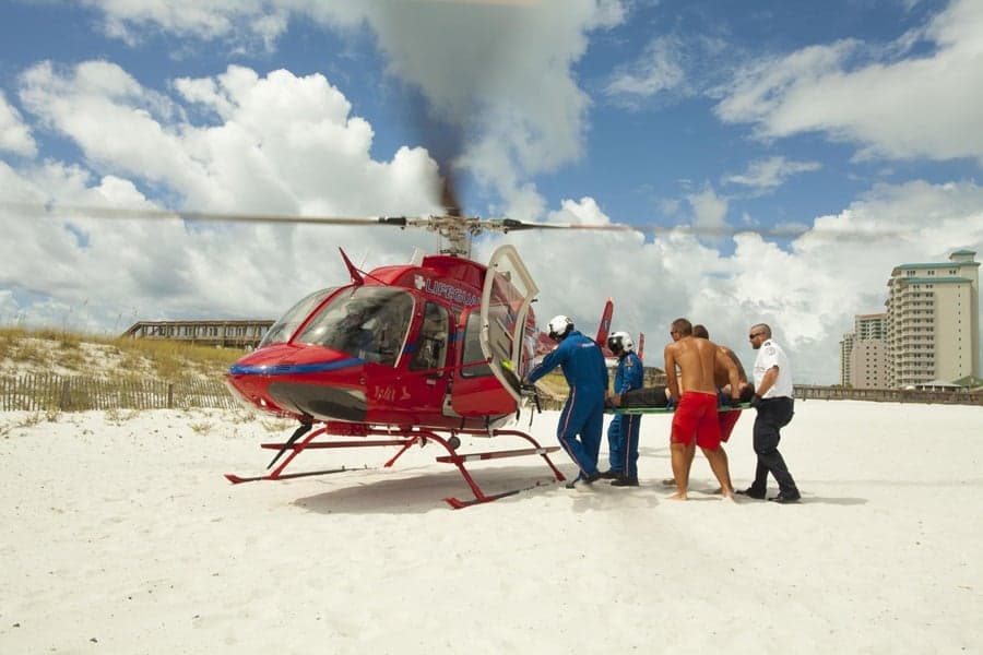 Air ambulance helicopter on a beach with medical personnel attending to a patient.