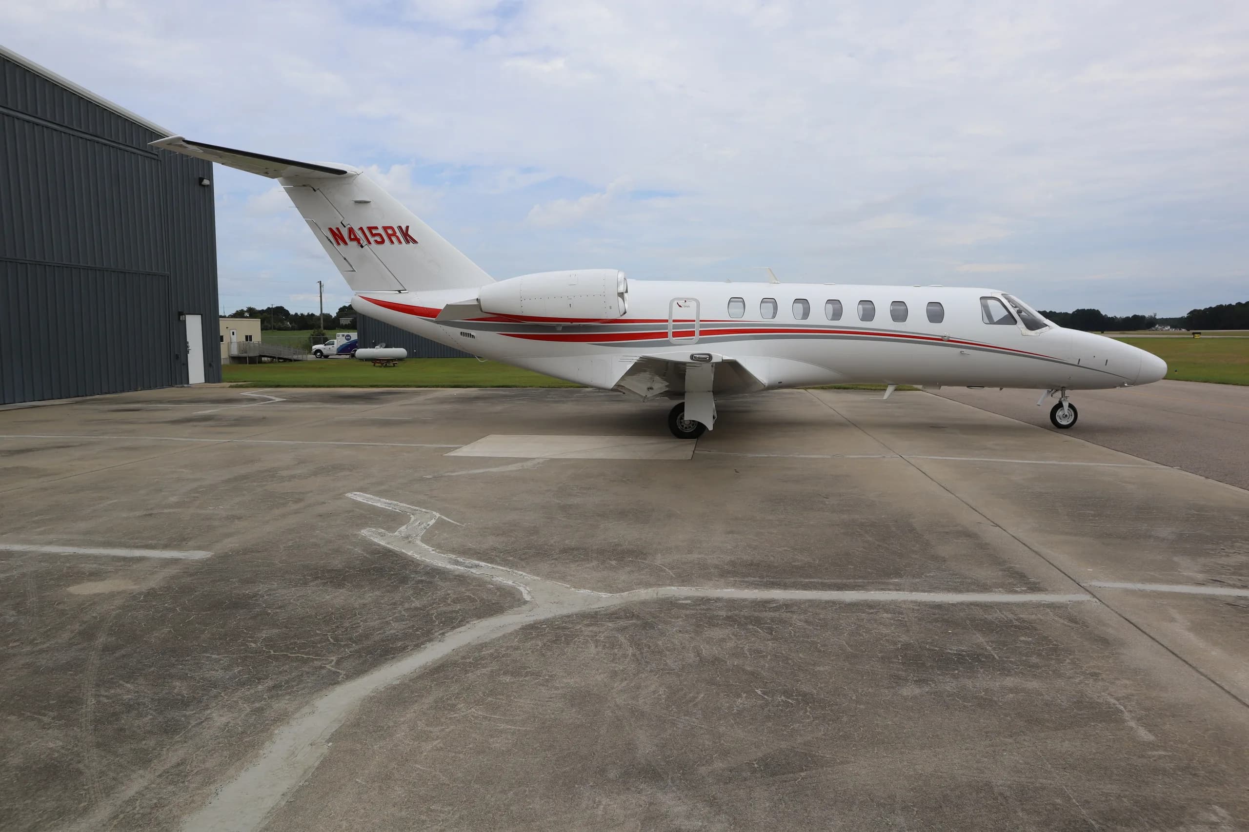 A three-quarter rear view of the white Cessna Citation business jet N415RK with red and grey stripes, parked on an tarmac.