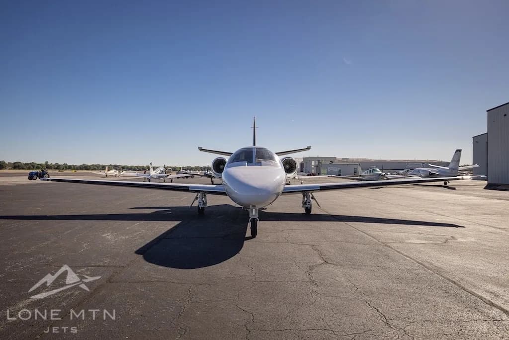 A head-on view of a white Cessna Citation Bravo business jet, tail number N700NR, parked on an airport tarmac with hangars in the background.