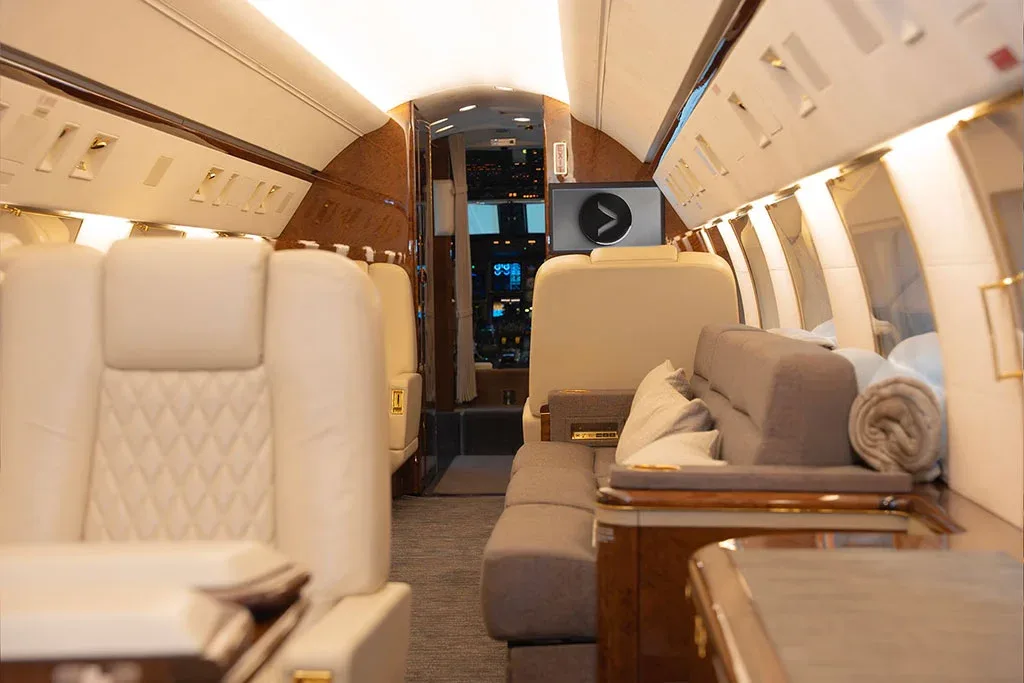 The private jet cabin features cream leather seats and a comfortable grey sofa with blankets.