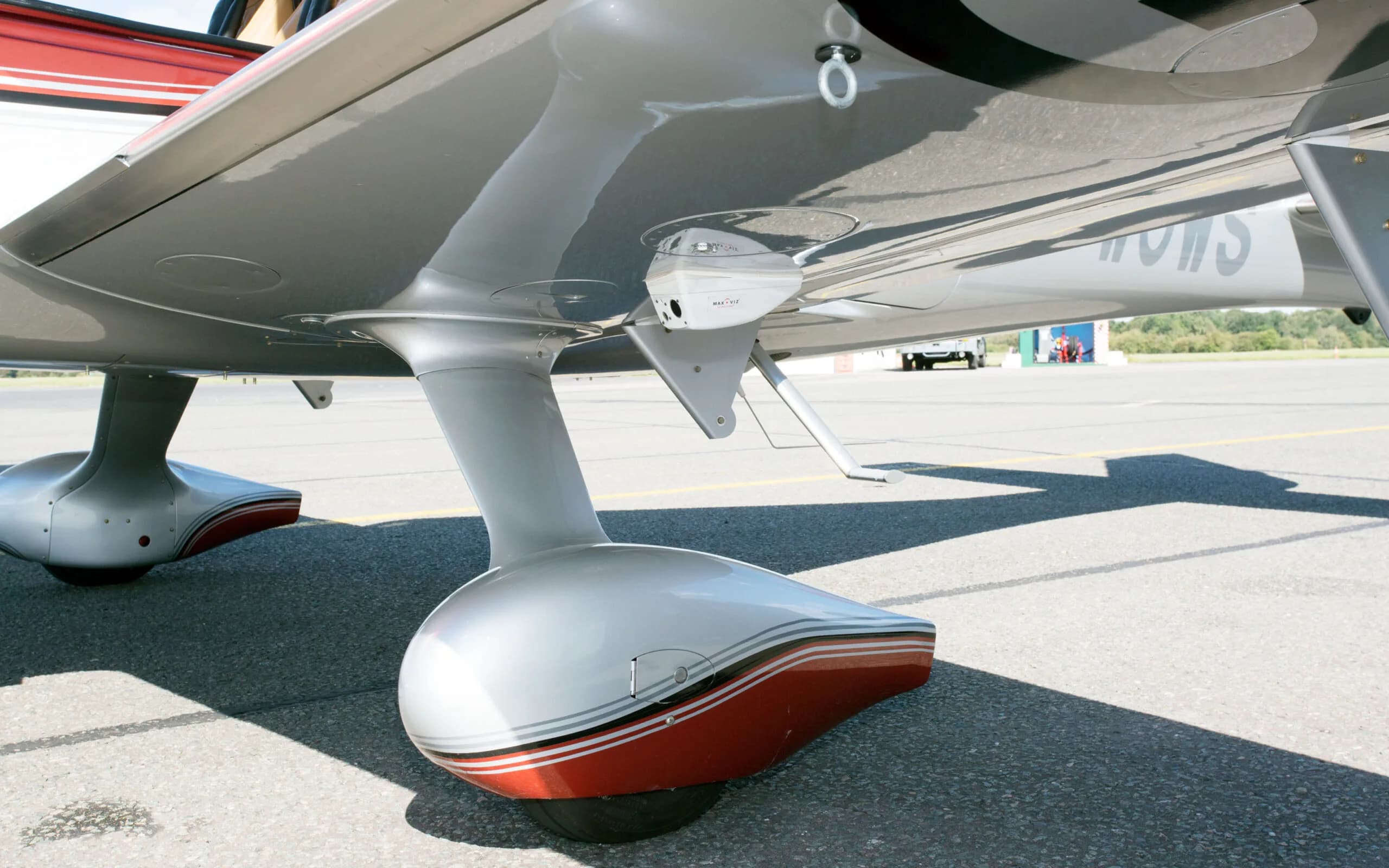 An underside view of a red and silver Cirrus SR22T GTS aircraft, showing the landing gear and a camera pod.