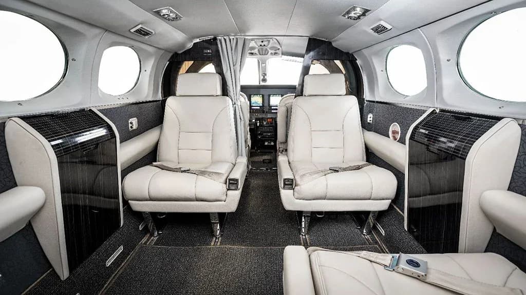 The aircraft's cabin interior features light-colored leather seats and dark patterned walls, looking towards the cockpit.
