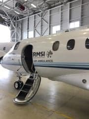 A white aircraft with RMSI Air Ambulance markings is parked in a hangar with the stairs down.