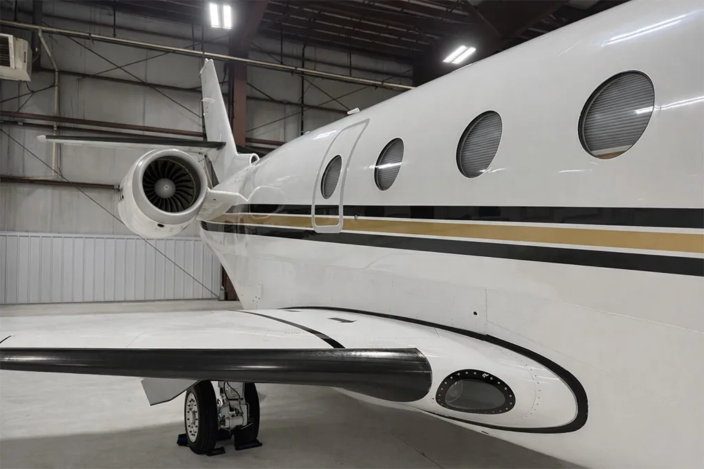 A close-up view of the rear fuselage, engine, and wing of a white Gulfstream business jet in a hangar.