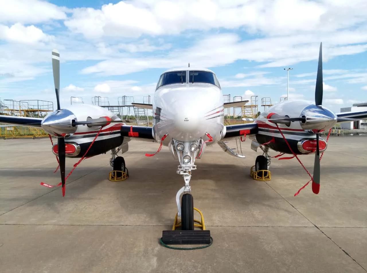 A King Air aircraft is parked on the tarmac with wheel chocks and propeller covers, front view.