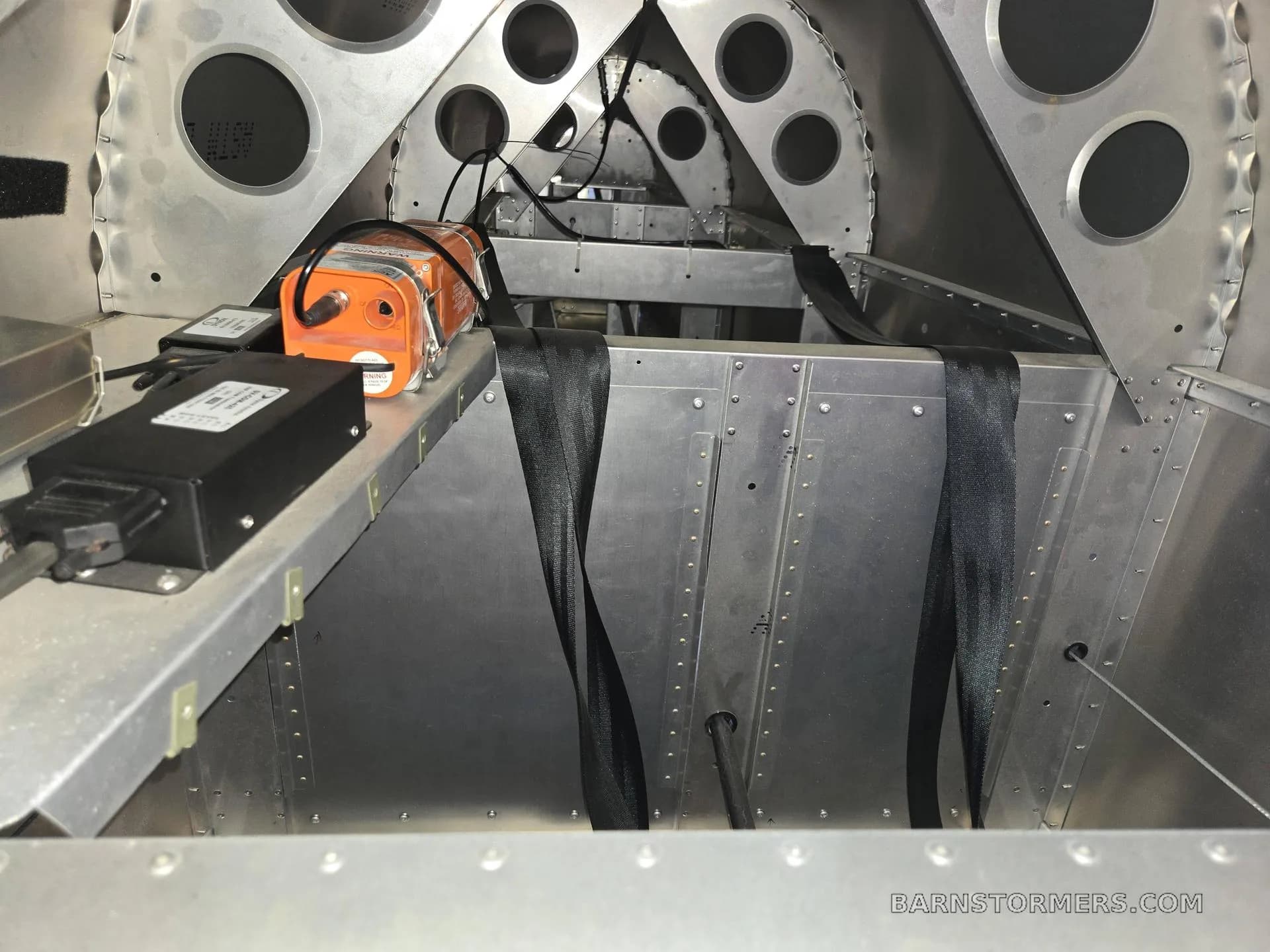 An interior view of an aircraft's aluminum fuselage structure with an orange box and black straps.