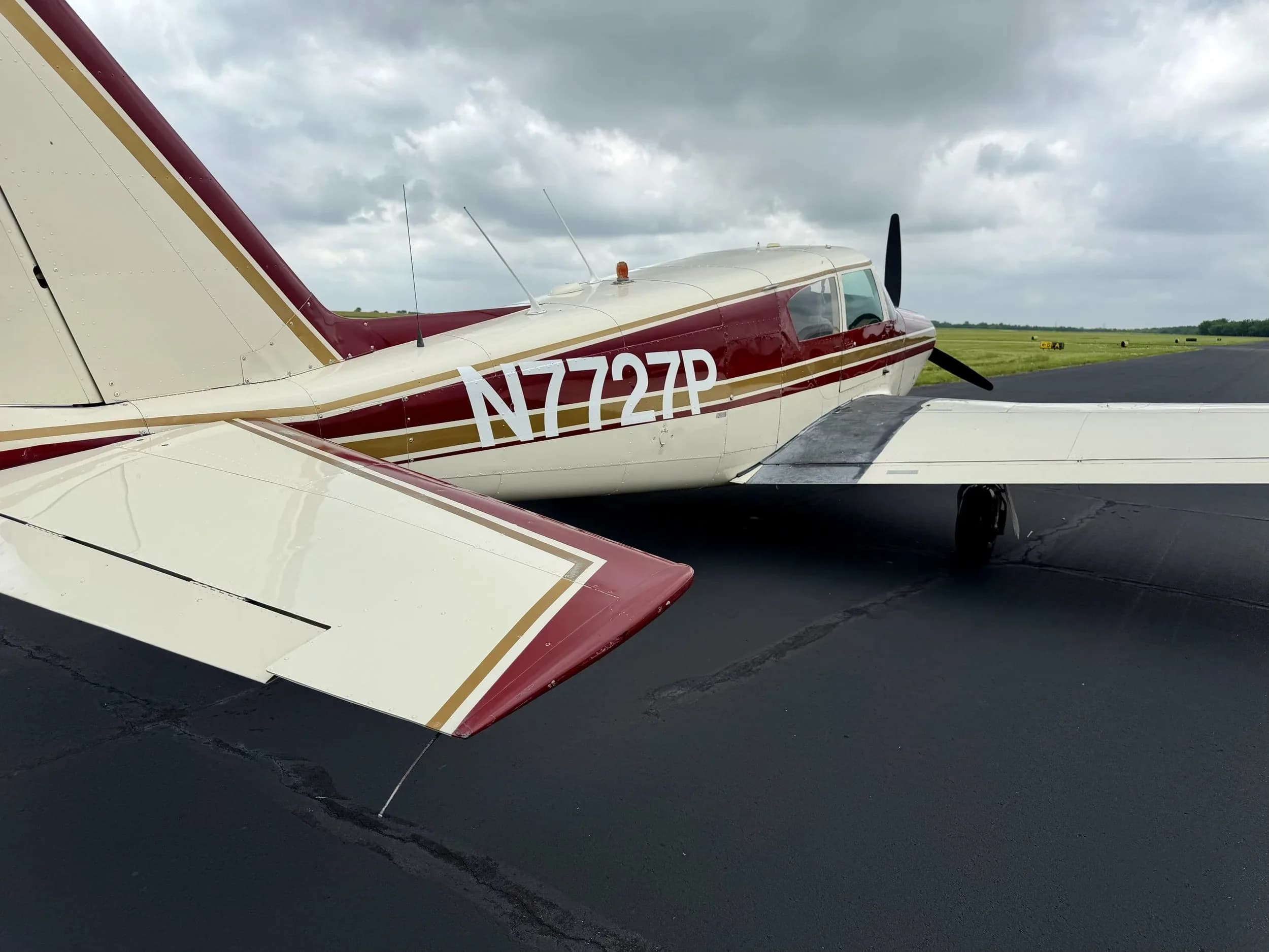 Rear-side view of a maroon and white Piper Comanche N7727P showing the tail and registration N7727P.