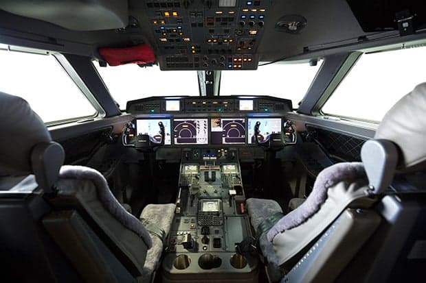 A wide view of a modern aircraft cockpit with multiple digital displays and pilot seats.