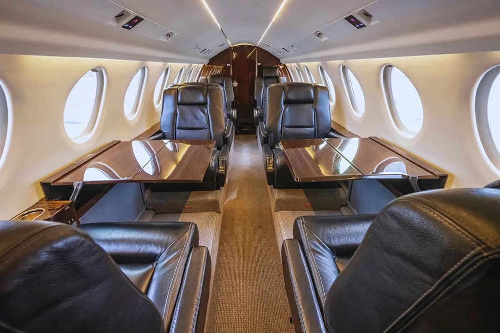 The luxurious interior cabin of a business jet, featuring black leather seats and polished wooden tables.