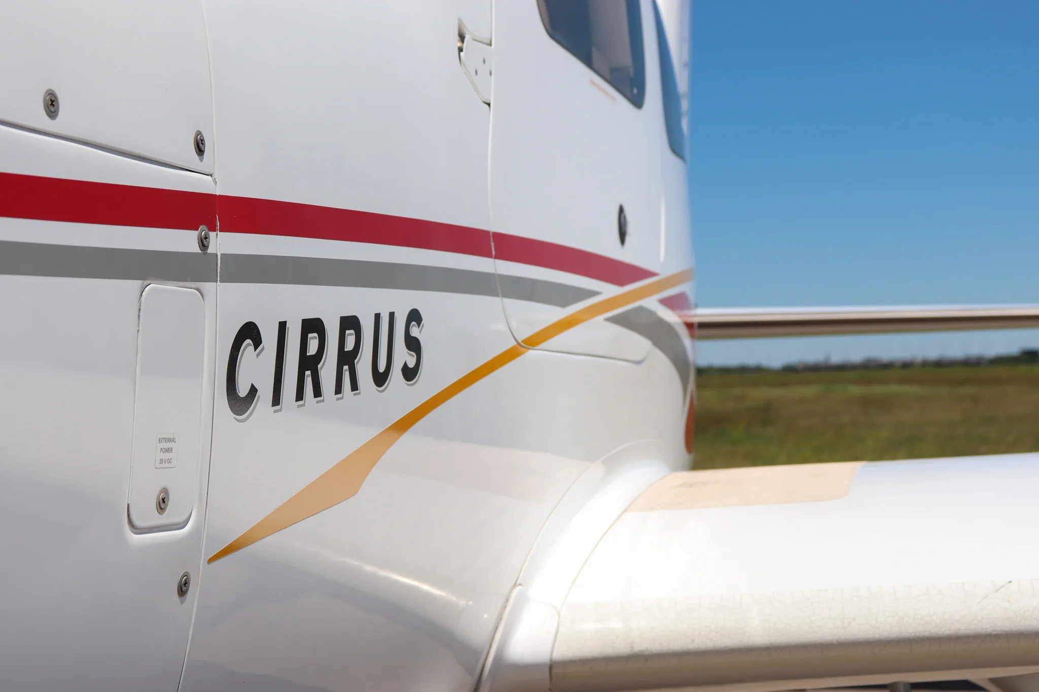 Close-up of the 'CIRRUS' text and red, grey, and gold stripe on the side of the aircraft fuselage.