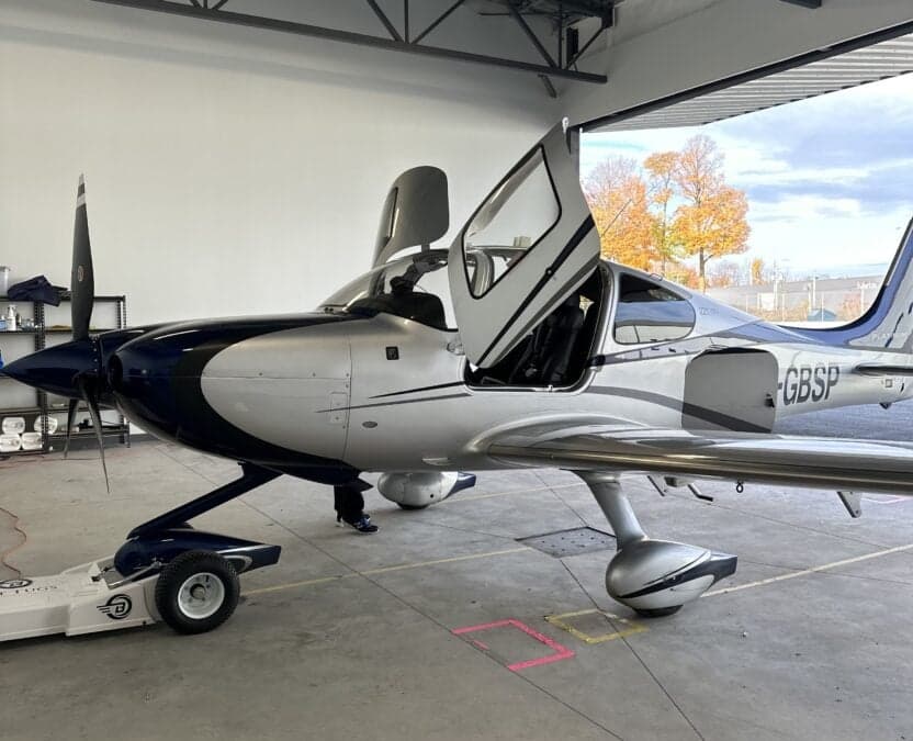 A Cirrus aircraft with open doors is being towed inside a hangar.