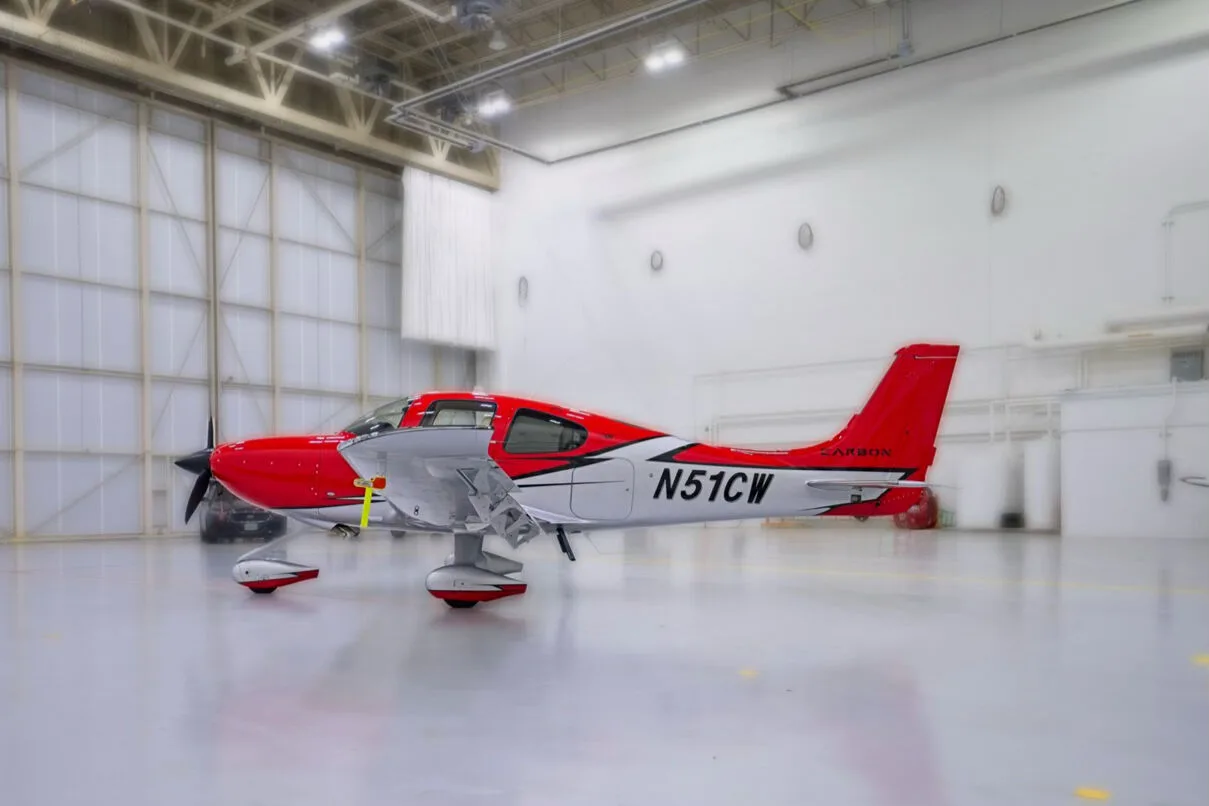 A red and white Cirrus SR22 aircraft with registration N51CW parked in a brightly lit hangar.