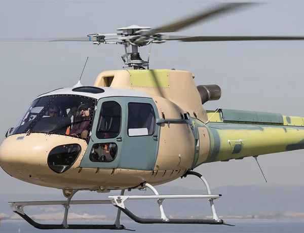 A helicopter in flight with a tan and green paint scheme.