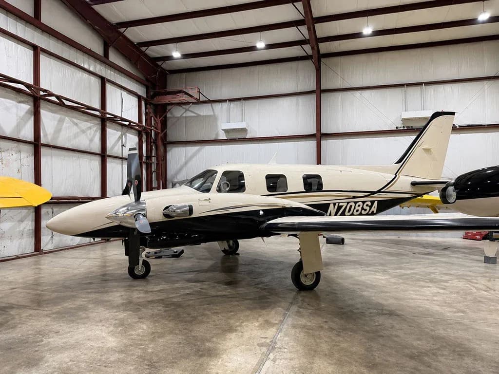 A side view of a white and black twin-engine propeller aircraft, N708SA, parked in a hangar.