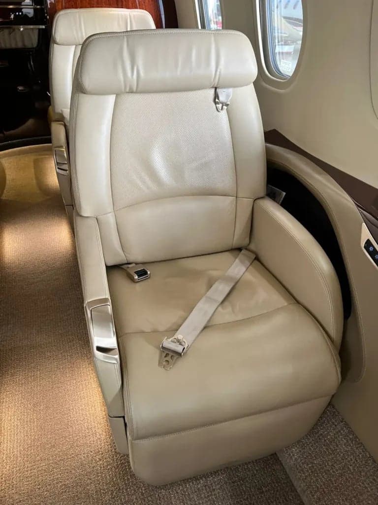 A single tan leather seat with a seatbelt in the aircraft cabin.