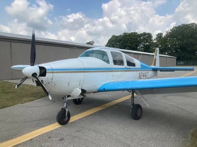 A white and blue single-engine propeller aircraft with registration N2441T is parked on an asphalt ramp in front of a hangar.