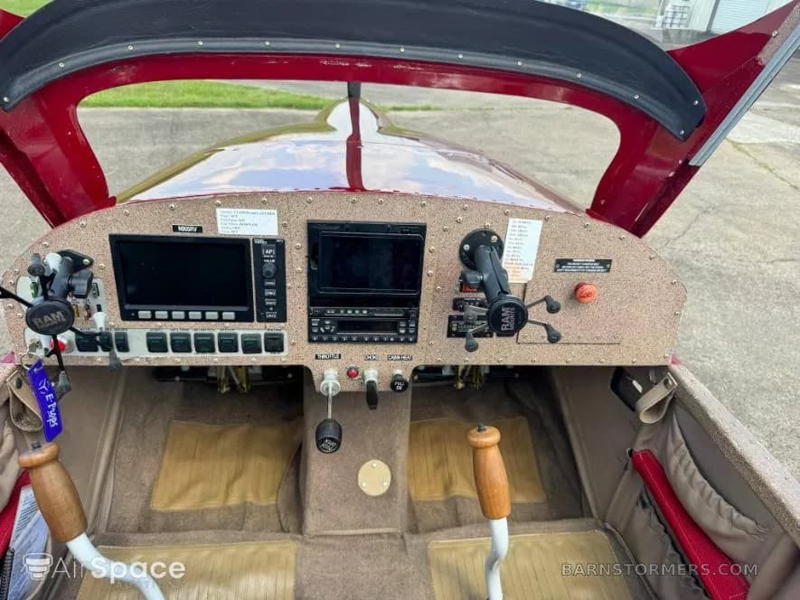 The cockpit of a red Vans RV-6 aircraft, showing the instrument panel with dual screens and controls.