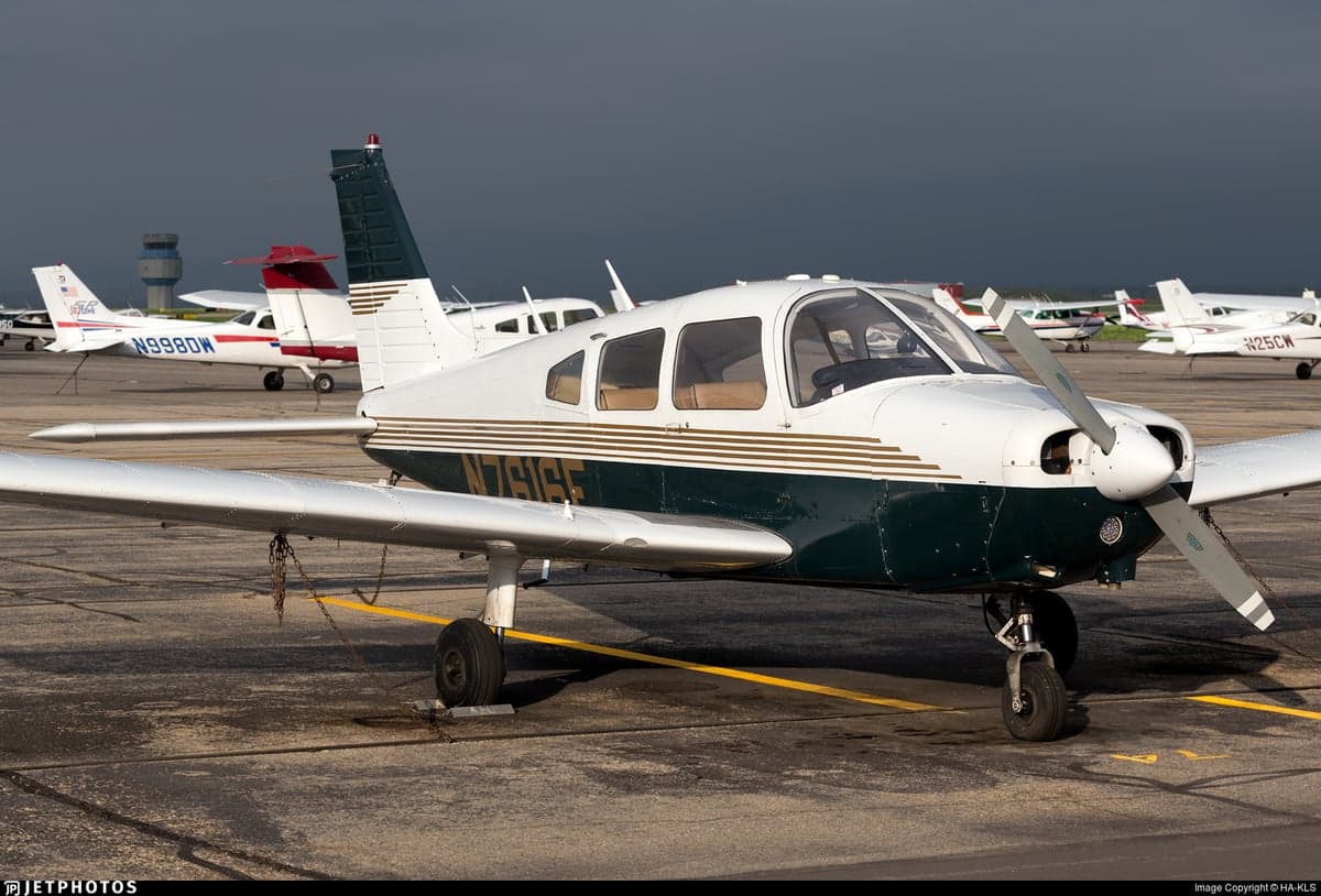 A Piper PA-28 Cherokee with a white and dark green paint scheme is parked on the tarmac.