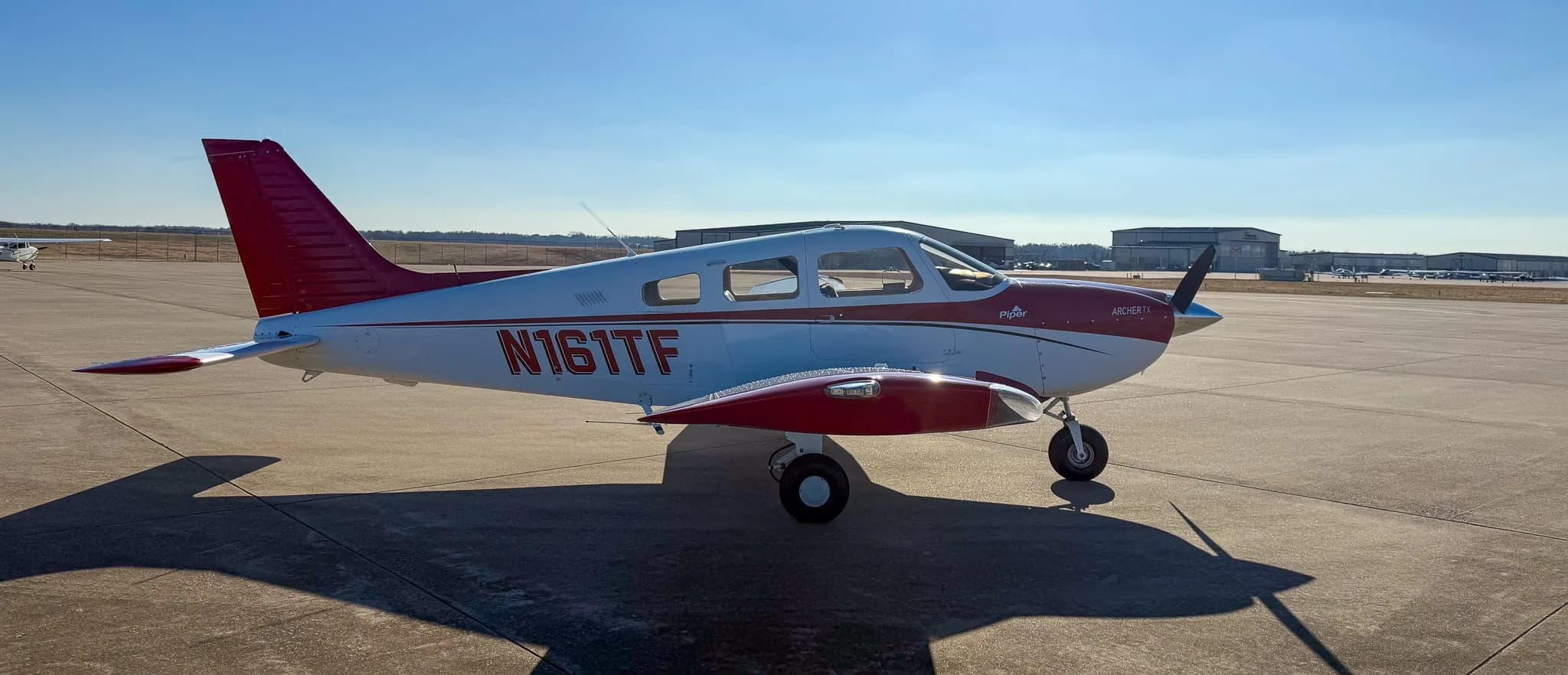 A side-right view of a red and white Piper Archer TX aircraft, tail number N161TF, parked on an asphalt tarmac.