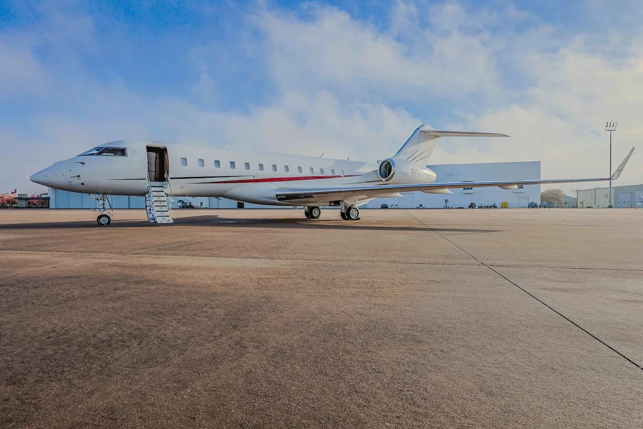 A white Bombardier Challenger business jet with red and black stripes on the tarmac, with its main door open and stairs extended.