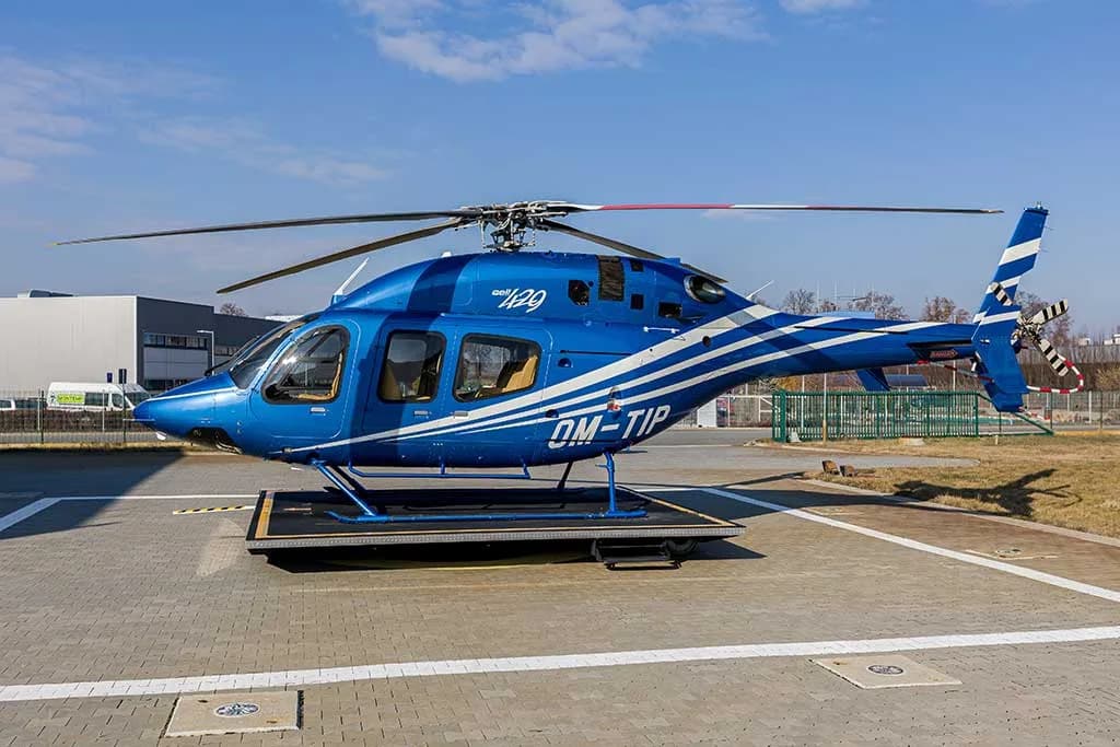 A side view of a blue helicopter with white stripes, registration OM-TIP, on a helipad.