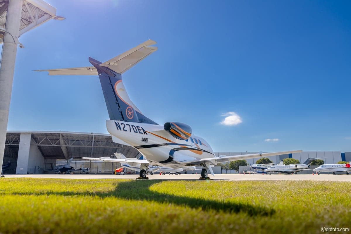 The tail of a Phenom 100 aircraft with registration N270EA parked on the grass.