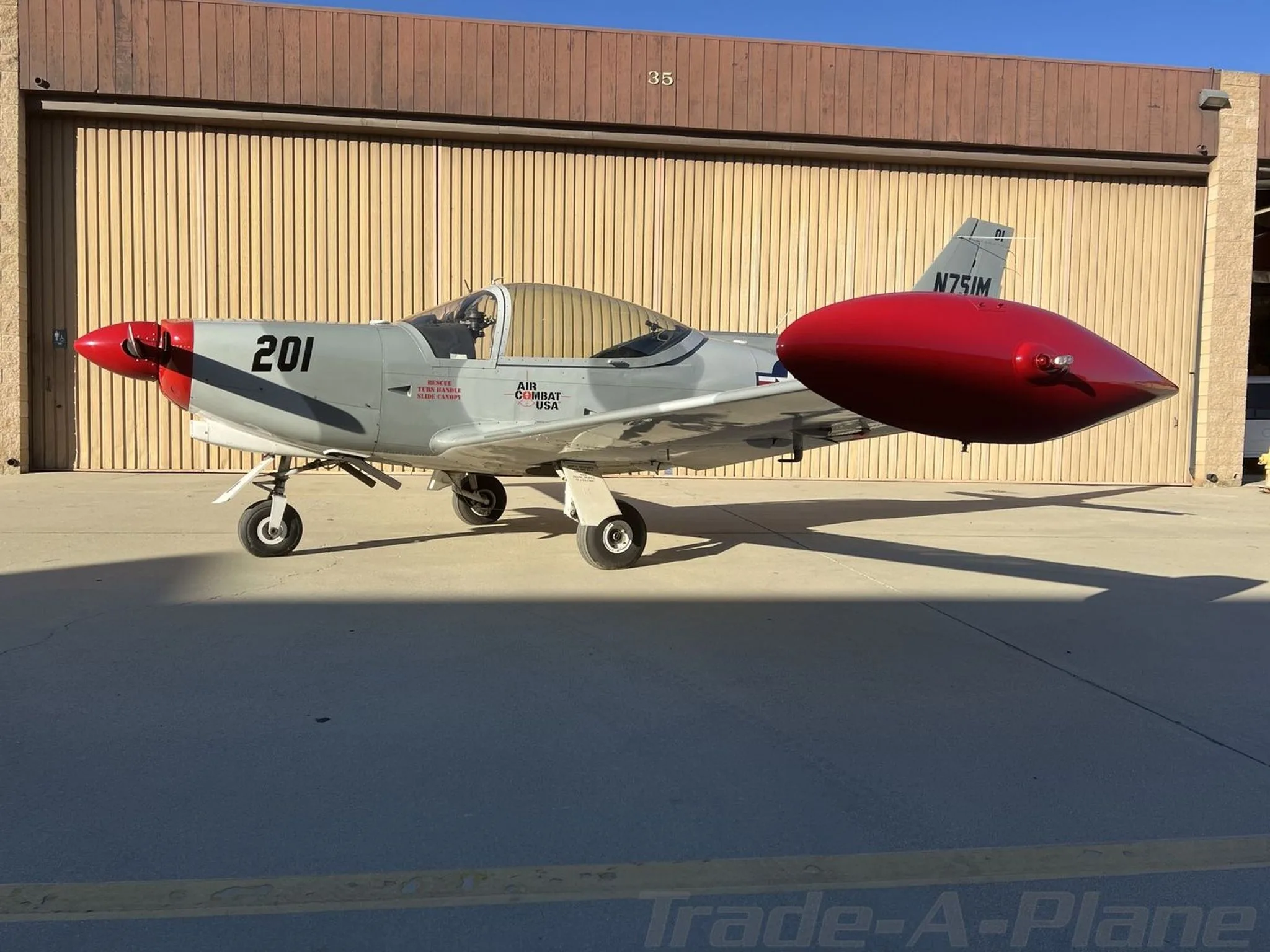 A side view of the grey and red Air Combat USA aircraft 'N751M' with a red external fuel tank.