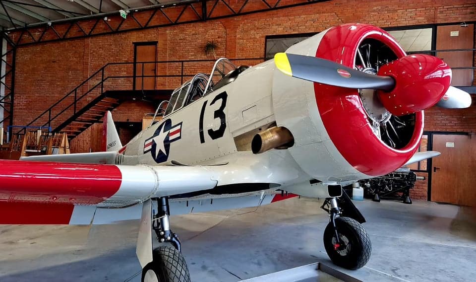 A white and red North American Aviation T-6 Texan aircraft is parked inside a building.
