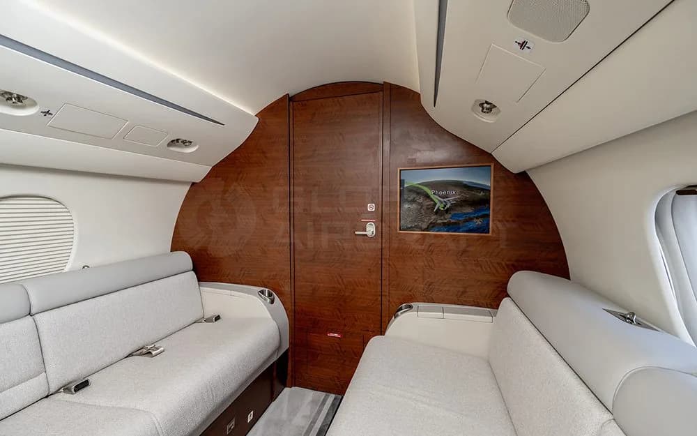 The rear section of a private jet cabin, featuring two gray sofas facing each other and a large wooden door.