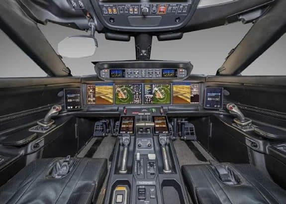 Aircraft cockpit with black leather seats and a modern instrument panel.