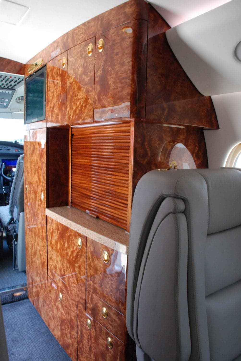 An aircraft cabin galley area featuring extensive wood cabinetry and a grey passenger seat.
