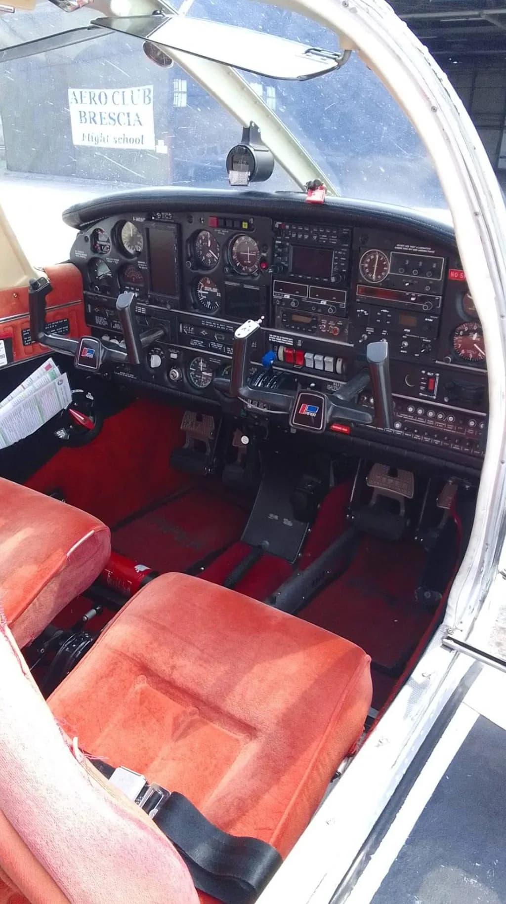 The cockpit of a Piper PA-28 aircraft with red seats and a view of the instrument panel and controls.