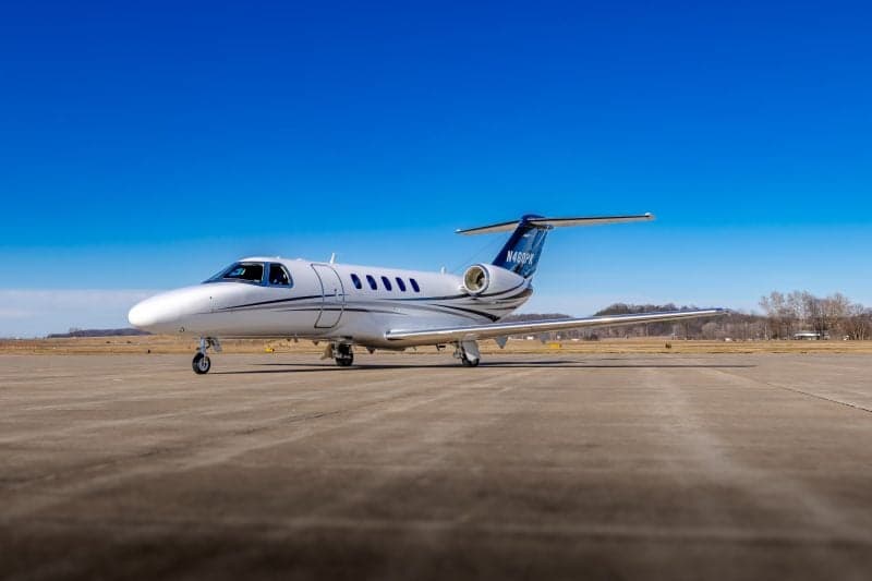 A white and blue Cessna Citation business jet with tail number N460PK is parked on an asphalt runway under a clear blue sky.