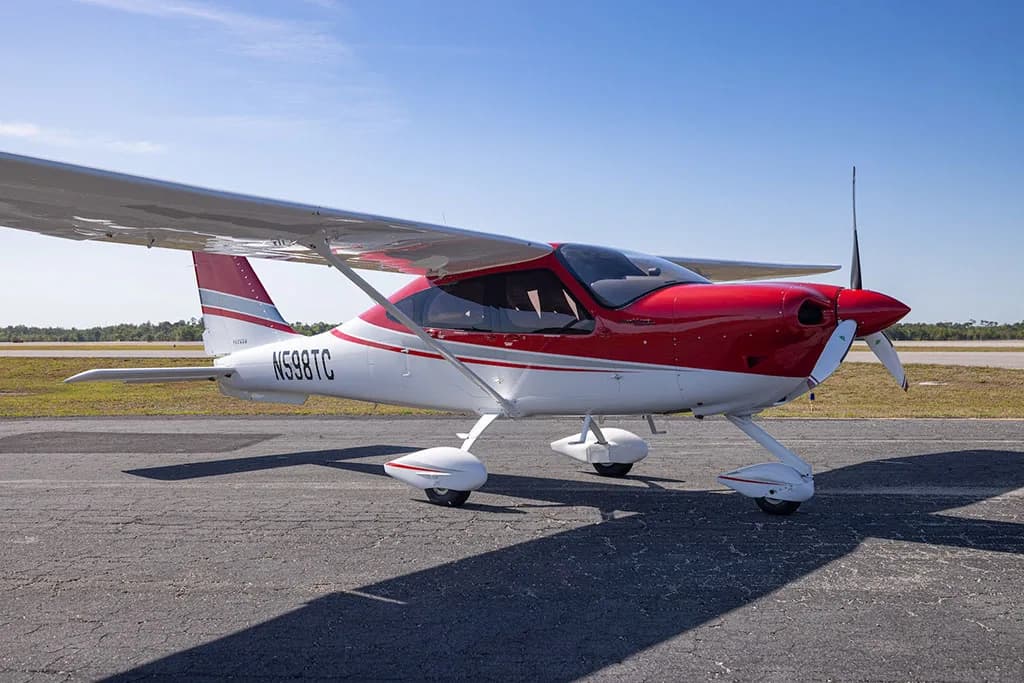 A front-side view of a red and white Tecnam P2010 aircraft with registration N598TC parked on an airfield.