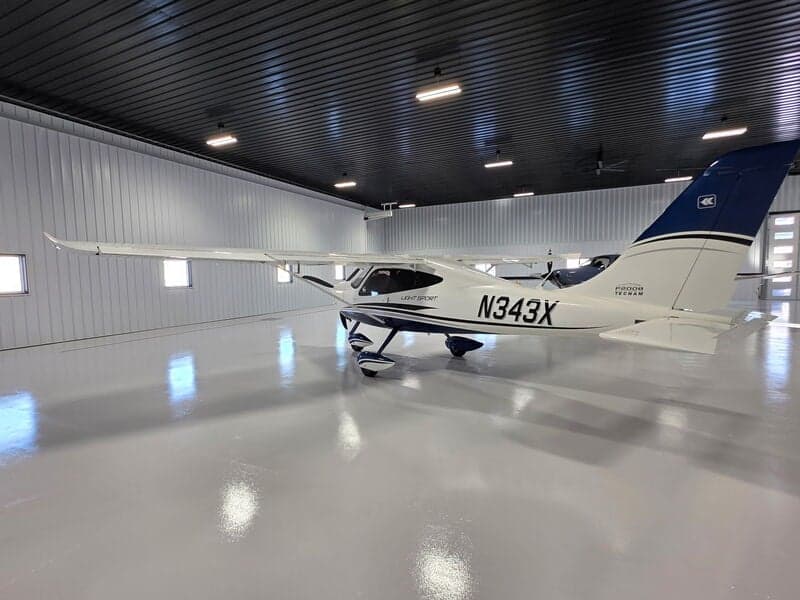 A white and blue Tecnam P2008 Light Sport aircraft (N343X) is parked in a hangar, viewed from the left side.