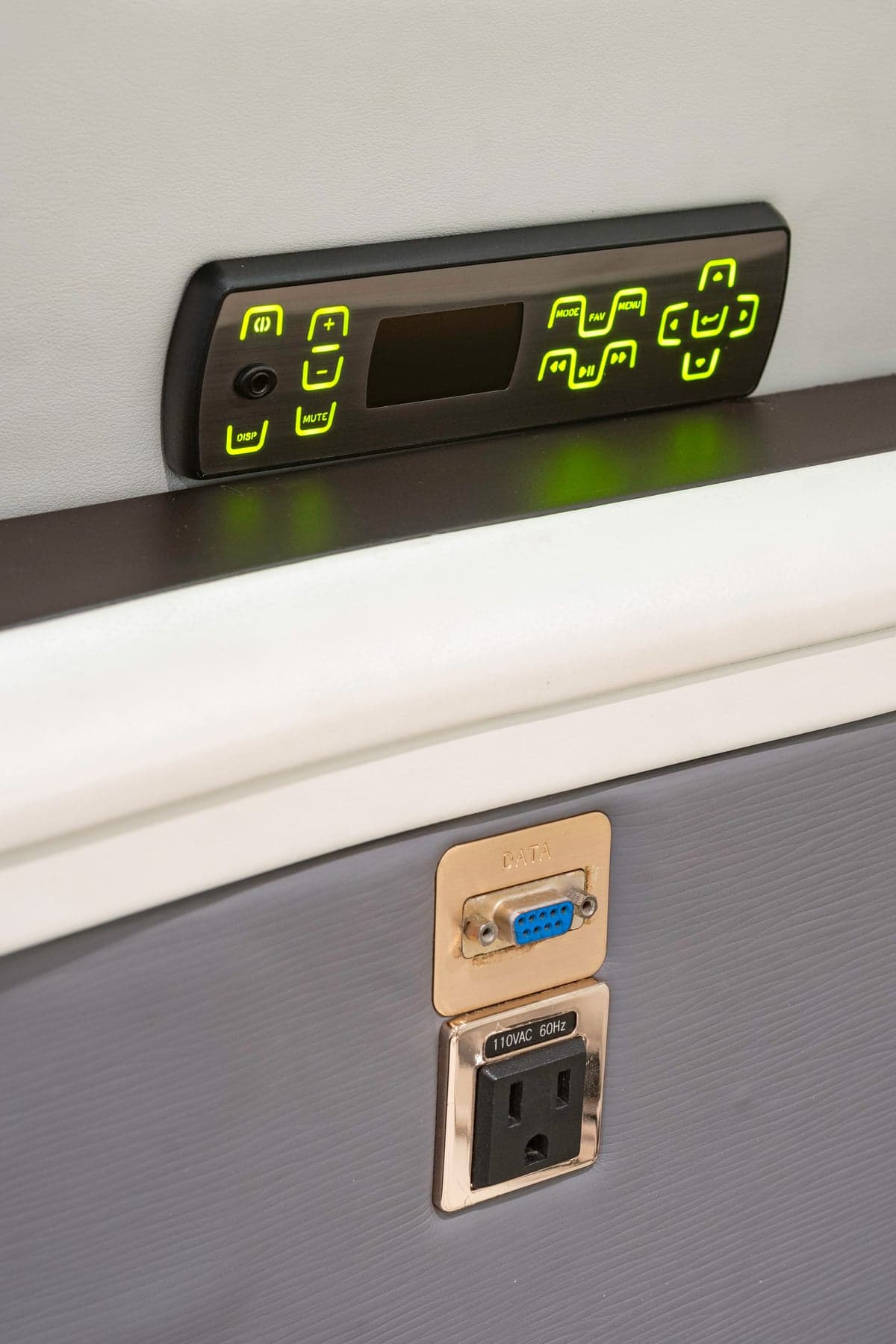 A close-up of an aircraft's cabin interior, showing an entertainment control panel and power outlets.