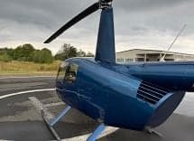A blue Robinson R44 helicopter on a helipad, viewed from the rear.