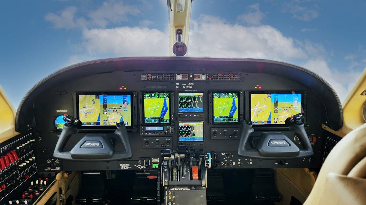 Wide view of an aircraft cockpit instrument panel with multiple displays and yokes.