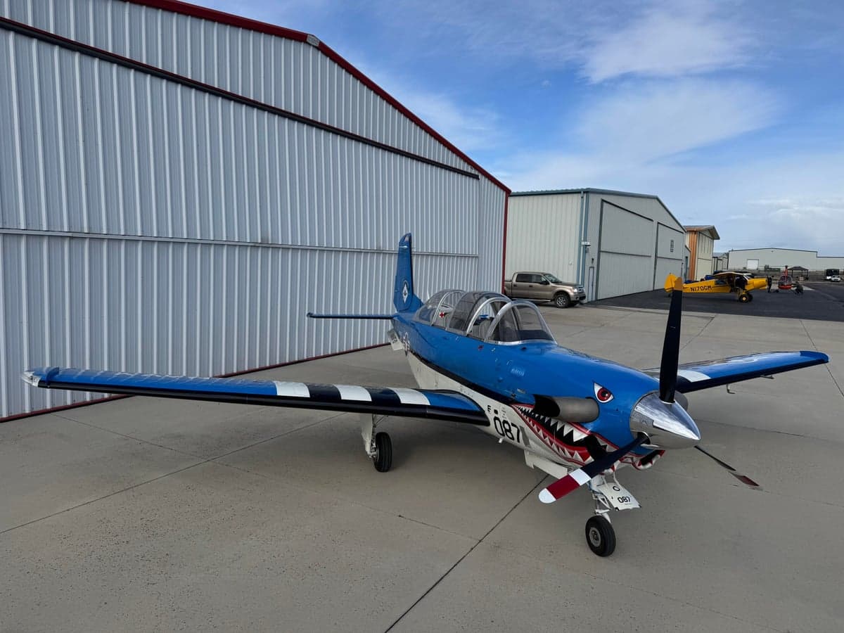 A blue and white SIAI-Marchetti SF.260 is parked on the tarmac with a shark mouth paint scheme.