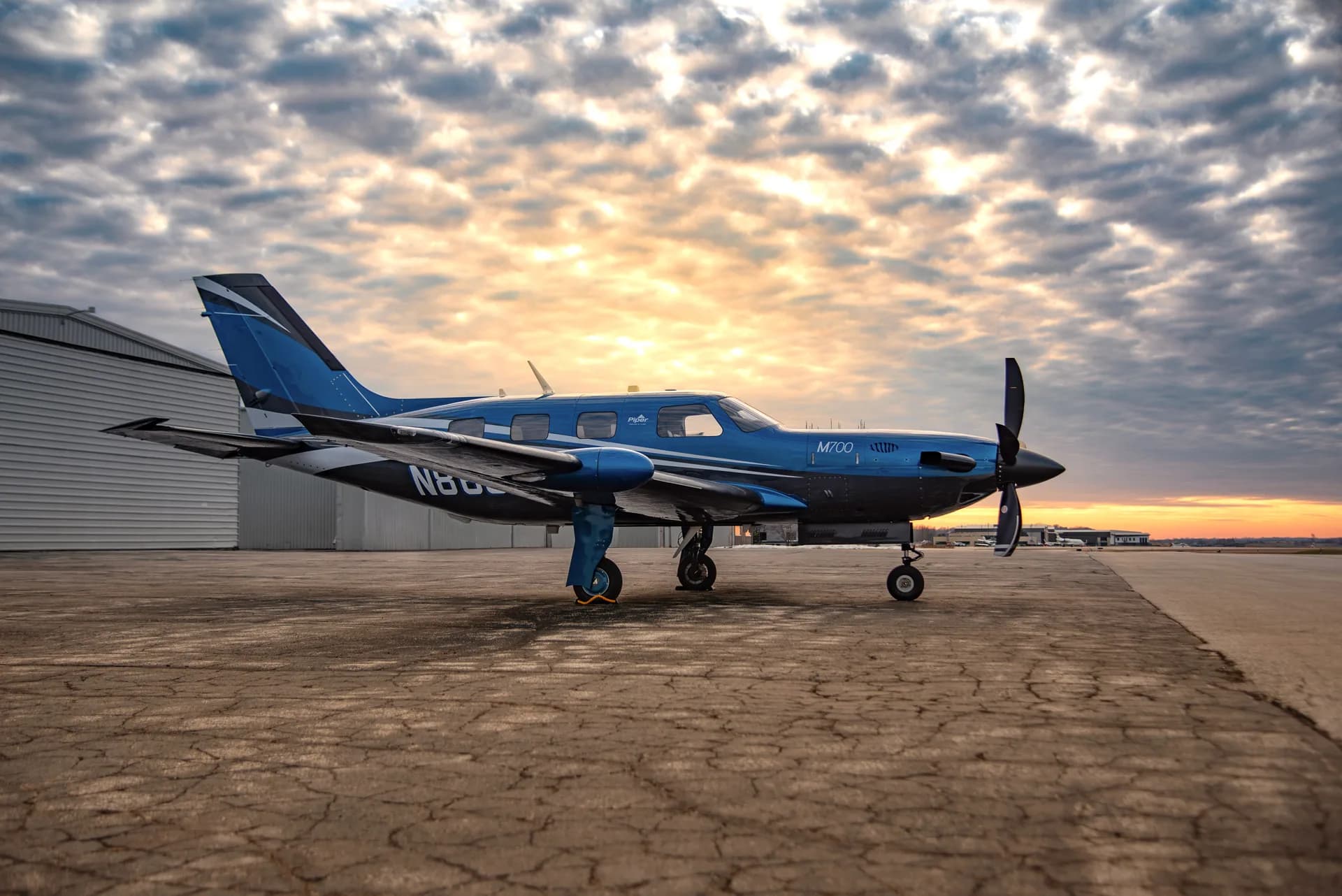 A blue and black M700 aircraft sits on the tarmac at sunset.