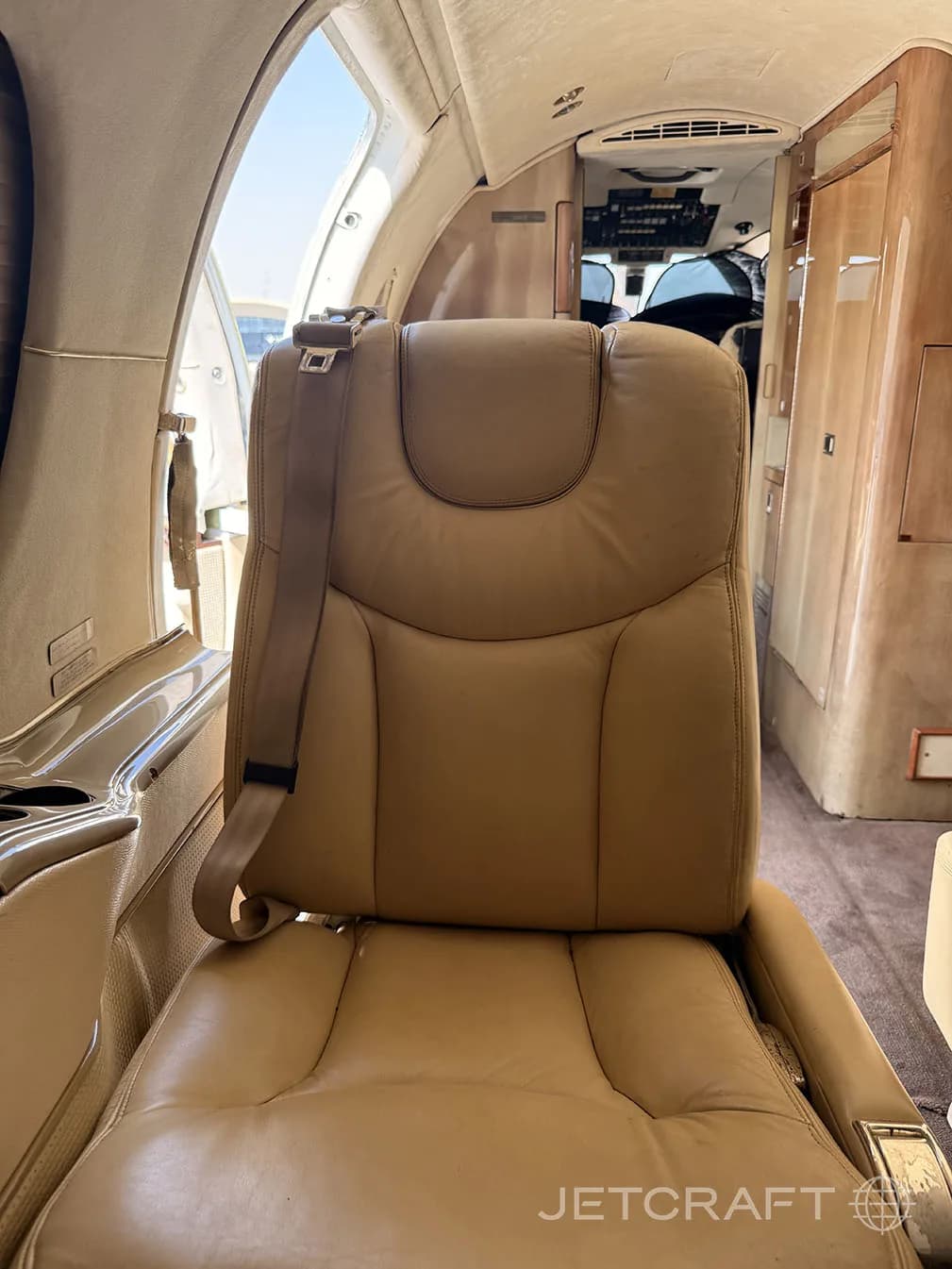 A tan leather seat in a private jet cabin, with an open door revealing the exterior.